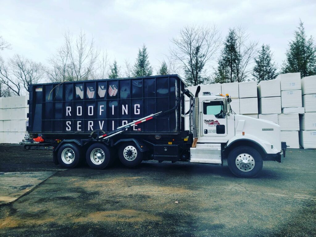 A commercial truck with a black and white trailer with "Roofing Services" written on the side along with the Tech Roofing logo