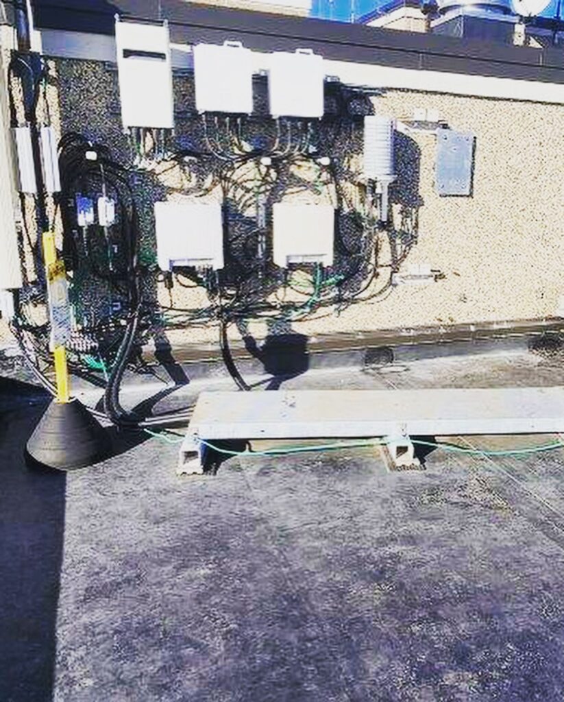 Close-up rooftop view of the Coes Pond Apartments EPDM roof replacement in Worcester, MA showing finished black membrane roofing around telecommunications equipment and cable supports.