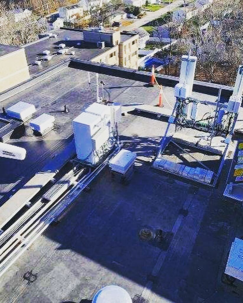 Close rooftop view of the Coes Pond Apartments EPDM roof replacement in Worcester, MA showing mechanical equipment, antenna structures, and finished black membrane roofing.